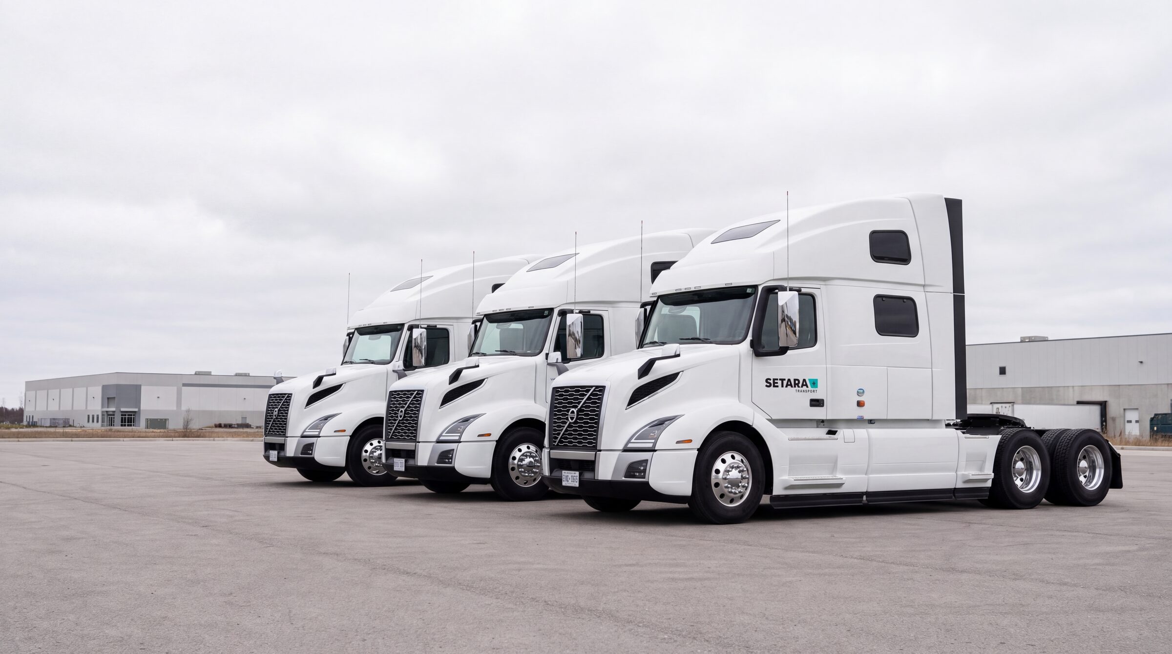 Three white truck tractors parked beside an industrial building