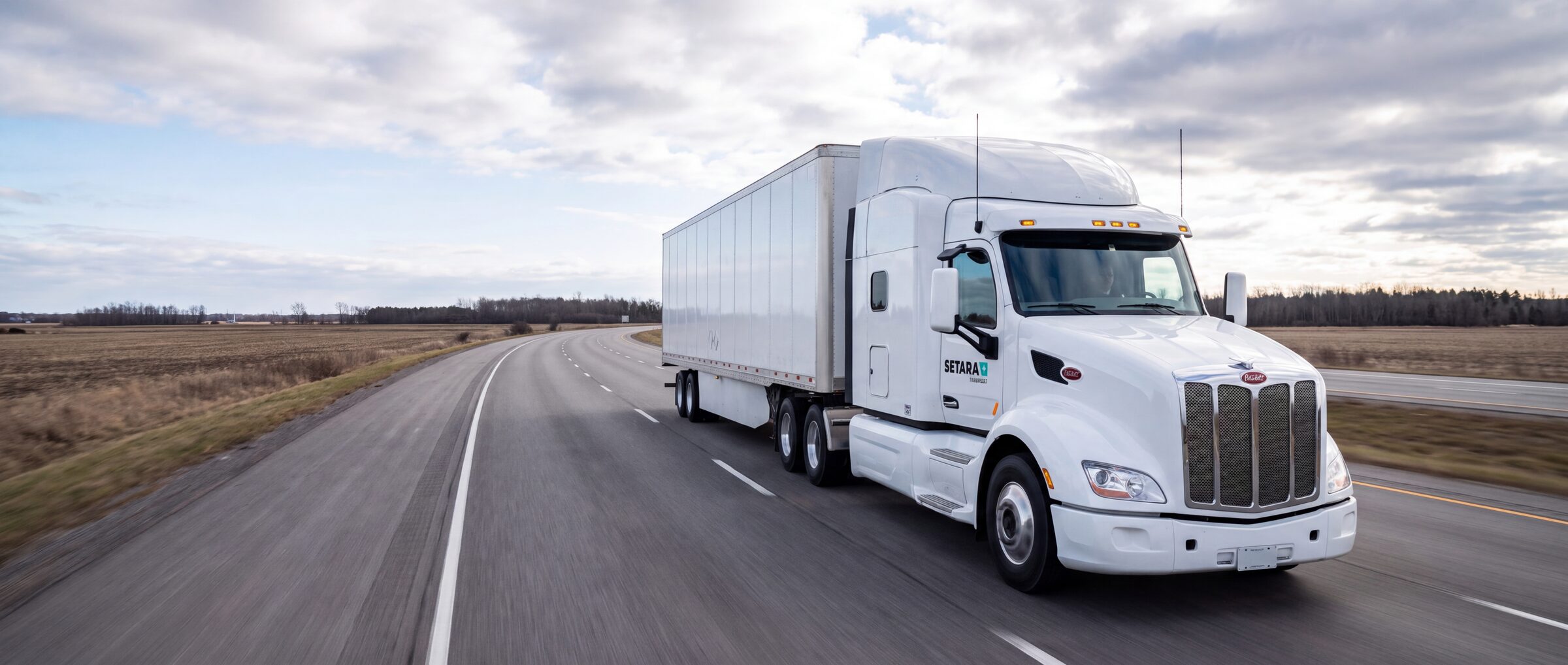 White tractor-trailer travelling on a rural highway